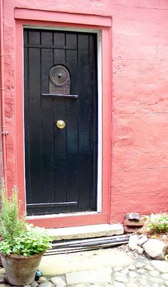 a potted plant sitting in front of a black door on a pink building with a round window