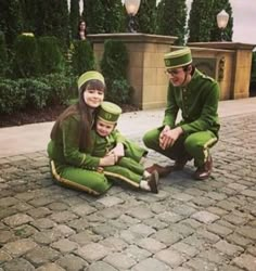 three people dressed in green sitting on the ground next to each other and posing for a photo