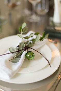 a white plate topped with green leaves and an olive branch on it's side