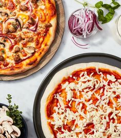 two pizzas sitting on top of pans covered in cheese and meat toppings