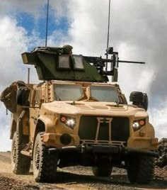 an army vehicle driving down a dirt road under a cloudy blue sky with clouds in the background