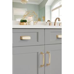 a bathroom with gray cabinets and white counter tops, gold pulls on the handles in front of the sink