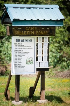 a sign that is in the grass near some bushes and trees with a blue roof