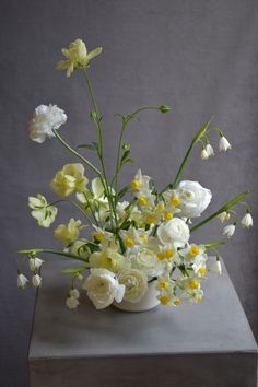 a vase filled with white and yellow flowers on top of a gray tableclothed surface