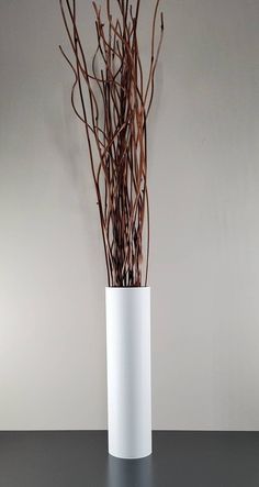 a white vase filled with branches on top of a black table next to a gray wall