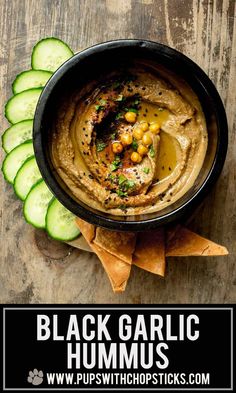 black garlic hummus in a bowl with cucumbers on the side