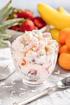 fruit salad in a glass bowl next to bananas, strawberries and pineapples