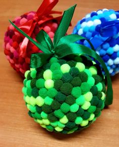 three pom - poms with green, blue and red bows on them sitting on a wooden surface