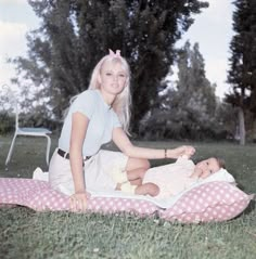 a woman sitting on top of a blanket next to a baby