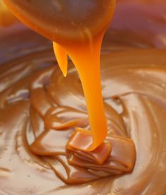 an orange liquid pouring into a bowl with peanut butter in it and caramel on top