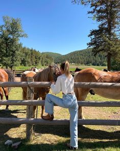 a woman leaning on a fence with horses in the background