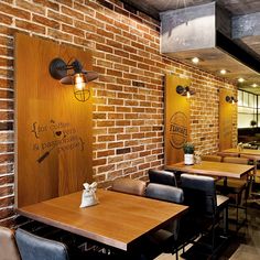 an empty restaurant with brick walls and wooden tables in the foreground, along with black leather chairs