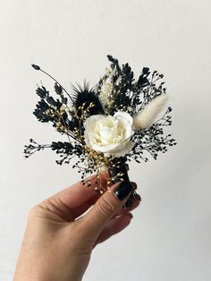 a hand holding a white and black boutonniere with dried flowers on it