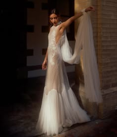 a woman in a white dress is standing near a brick wall