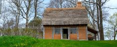 an old thatched roof house in the middle of a grassy field with trees and flowers