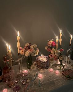 a table topped with lots of candles next to a cake and wine bottles on top of a table