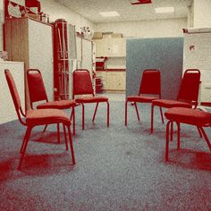 several red chairs are in a room with blue carpet and white walls, one is empty