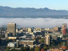 the city is surrounded by tall buildings and fog in the valley below it, with mountains in the distance