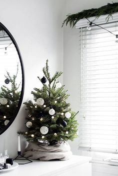 a small christmas tree sitting on top of a white dresser next to a mirror and window