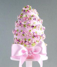 a three tiered cake decorated with pink flowers and bows on a white stand in front of a gray background