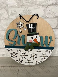 a wooden sign that says let it snow with a snowman wearing a top hat