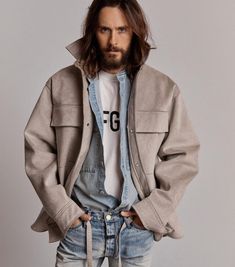 a man with long hair wearing a jacket and jeans