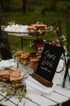 a table topped with lots of desserts next to a forest filled with grass and flowers