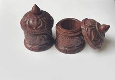 two wooden containers sitting next to each other on a white counter top, one has a lid and the other has an intricately carved design