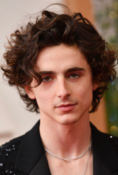 a young man with curly hair wearing a black shirt and silver necklace on his neck