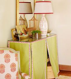 a green cabinet with two lamps on top of it next to a chair and mirror