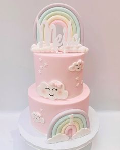 a three tiered pink cake with rainbows and clouds on the top is decorated in fondant