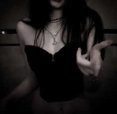 a woman in a black top is making the peace sign with her hands while wearing a necklace