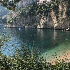 people are swimming in the clear blue water near some cliffs and houses on top of a hill