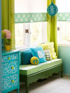 a living room with green curtains, blue and yellow furniture and flowers on the window sill