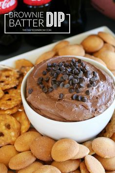 a bowl of chocolate dip surrounded by cookies and pretzels on a platter