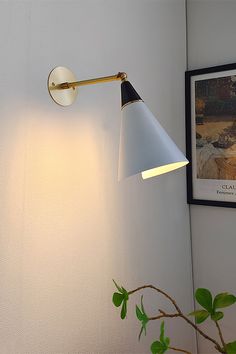 a white wall mounted light next to a plant on a table with a framed photograph