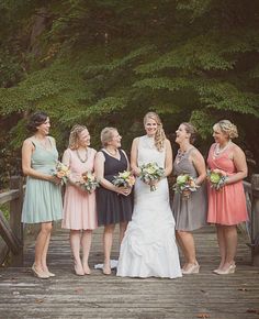 a group of women standing next to each other on a wooden bridge holding bouquets