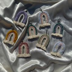 six pairs of earrings with tassels are on a white fabric background, one is shaped like a rainbow