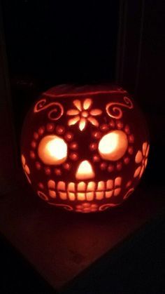 a pumpkin carved to look like a skull with glowing eyes and flowers on its face