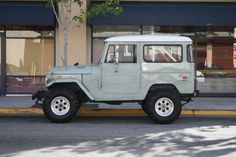 a green jeep is parked on the side of the road in front of a store