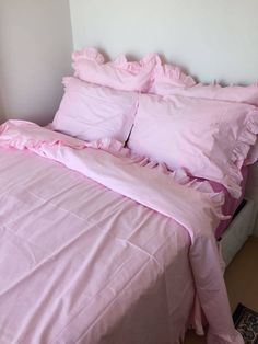 a bed with pink sheets and pillows on top of it in a room that has white walls