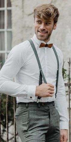 a man wearing a bow tie and suspenders standing in front of a fence with his hands on his hips