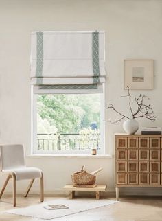 a living room with white walls and wooden furniture in front of a window that has roman shades on the windowsill