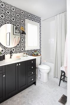 a bathroom with black and white wallpaper on the walls, a round mirror above the toilet