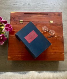 a pair of glasses and a book are on a wooden tray next to a flower