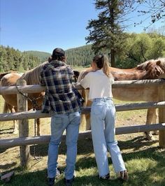 a man and woman standing next to a fence with horses in the background on a sunny day