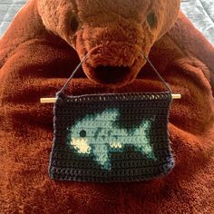 a teddy bear is holding a crocheted bag with a fish on it's side