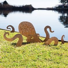 two metal octopus sculptures sitting in the grass near water's edge, one with its mouth open