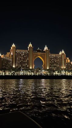 a large building sitting on top of a river next to a tall bridge at night