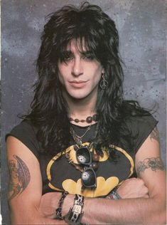 a man with long hair wearing a batman shirt and bracelets, posing for a photo